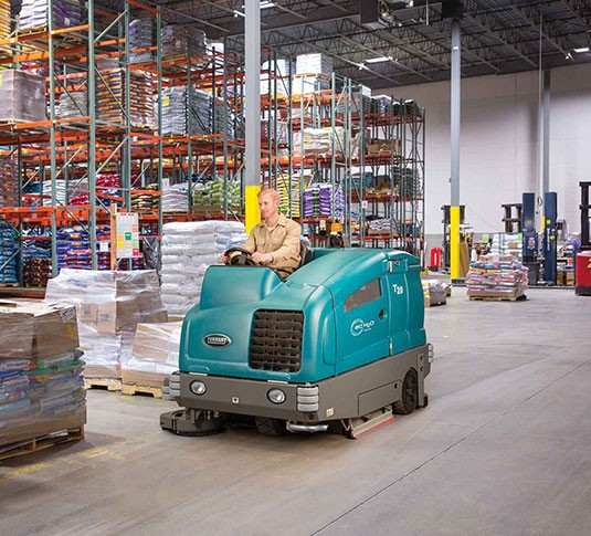 T20 Industrial Rider Floor Scrubber scrubbing a warehouse floor.